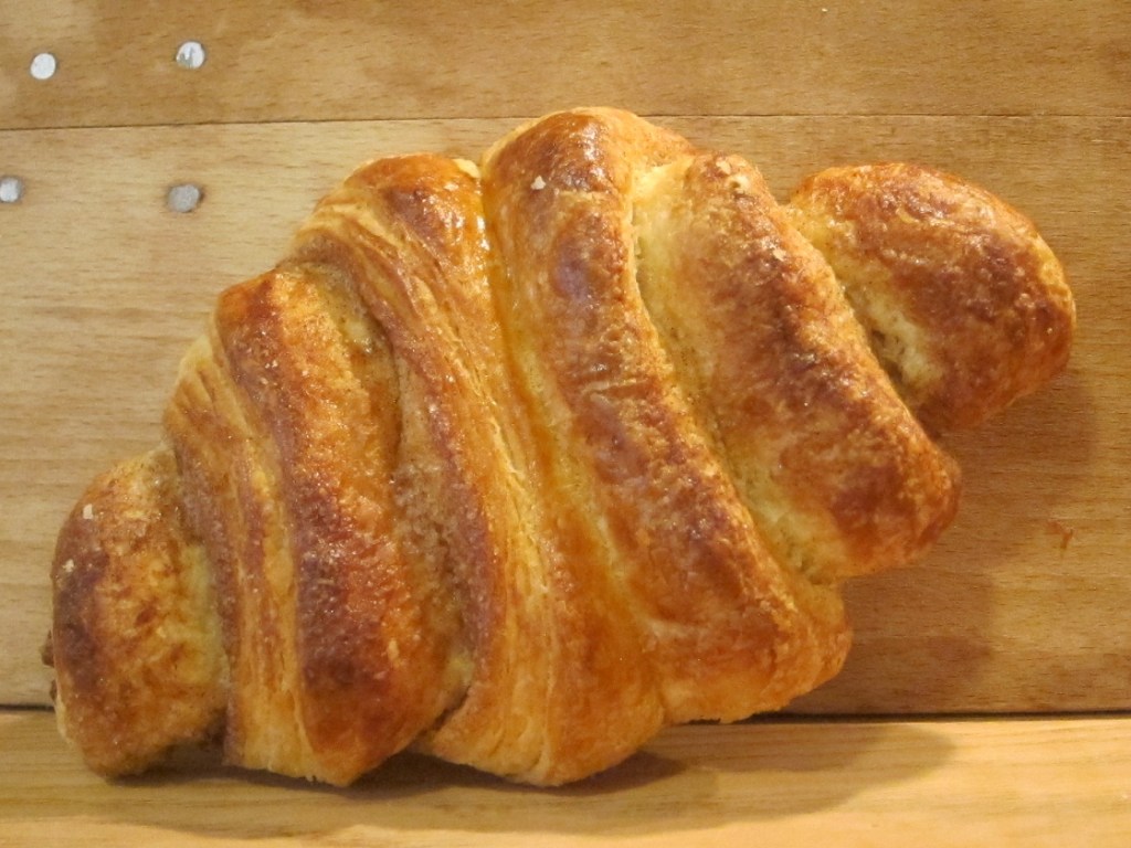 Ein frisch gebackenes Croissant auf einem Holzbrett.