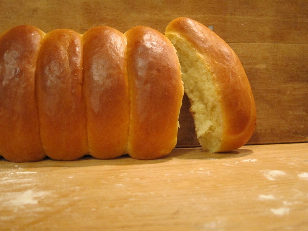 Ein frisch gebackenes, golden-braunes Briochebrot, mit einer Scheibe, die teilweise herausgeschnitten ist, auf einer Holzoberfläche.