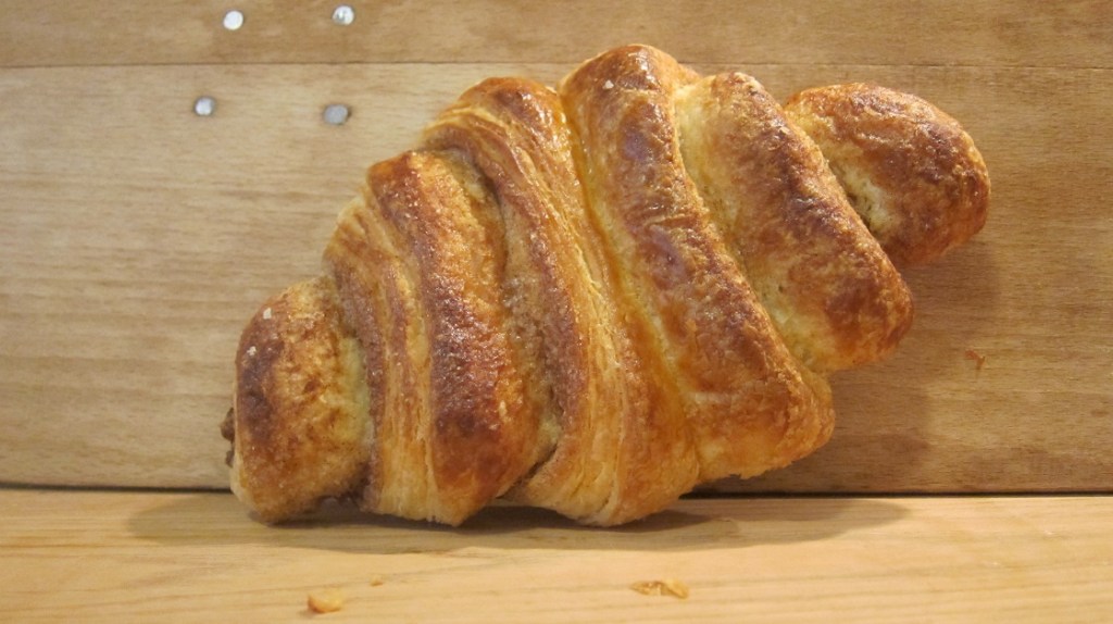 Frisch gebackenes Croissant aus Hefeteig, auf einem Holzbrett platziert.