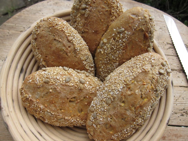 Ein Korb mit mehreren rundlich geformten Brötchen, die mit Sonnenblumenkernen und Haferflocken bestreut sind.