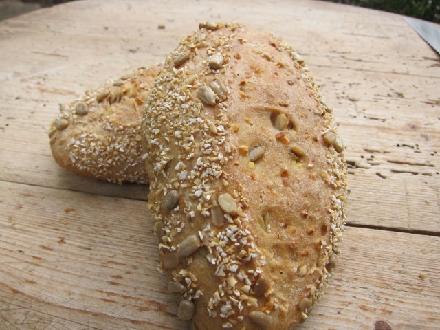 Zwei rustikale Brötchen mit Sonnenblumenkernen und Haferflocken auf einer Holzoberfläche.
