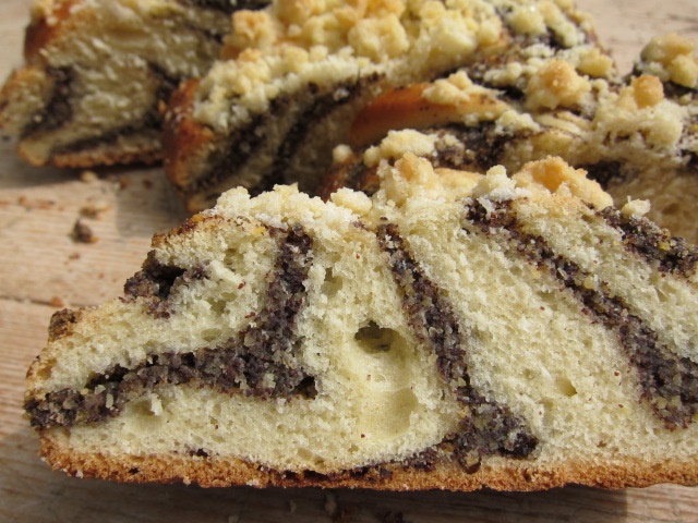 Z slice of sweet poppy seed bread with a crumbly topping, showcasing a marbled interior of sweet dough and poppy filling.
