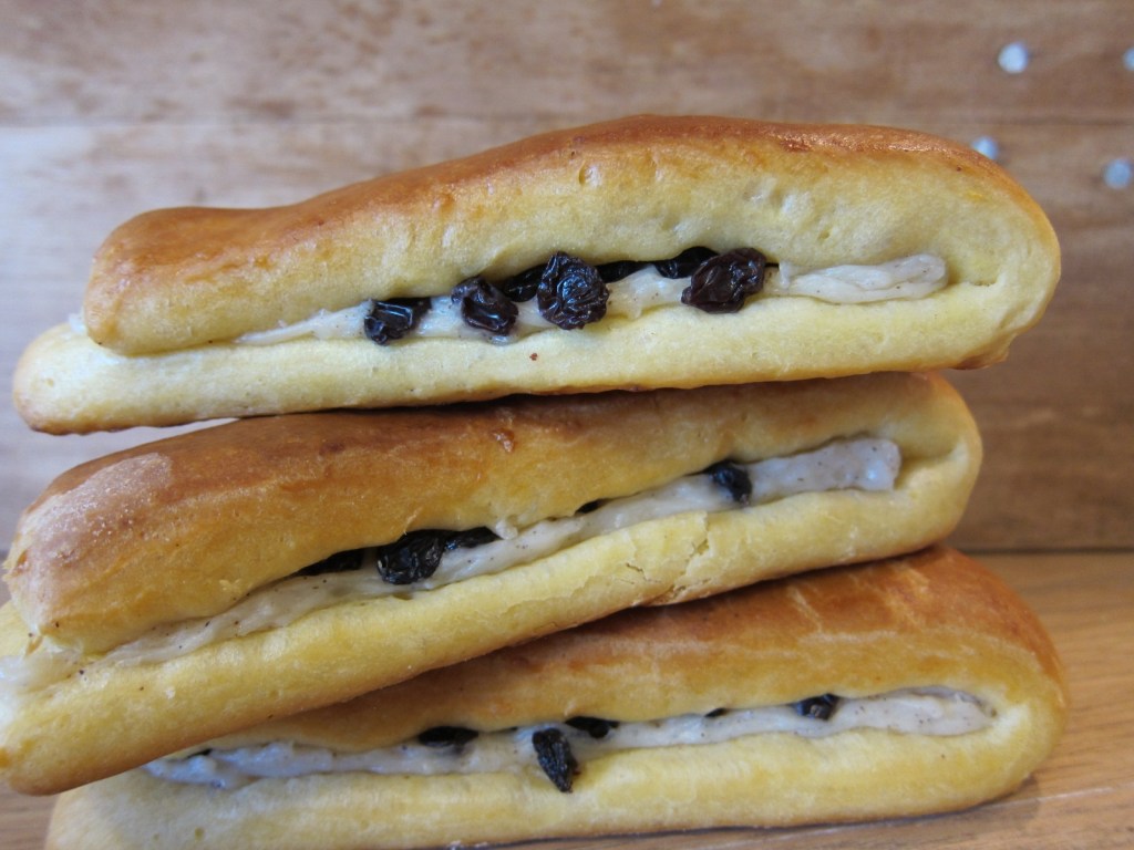 Drei gestapelte, gefüllte Hefeteiggebäcke mit einer cremigen Füllung und Rosinen.