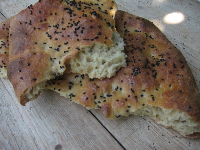 Zwei Stücke Fladenbrot mit schwarzen Sesamsamen, auf einem Holzuntergrund.