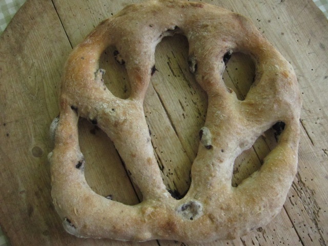 Rundes Fladenbrot mit offenen Löchern und einer rustikalen Oberfläche, auf einem Holzbrett platziert.