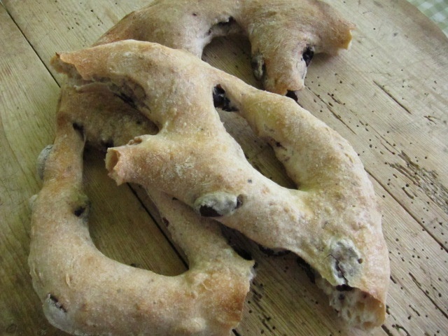 Drei rustikale, handgemachte Brote auf einem Holzbrett, leicht krümelig und mit goldbrauner Kruste.