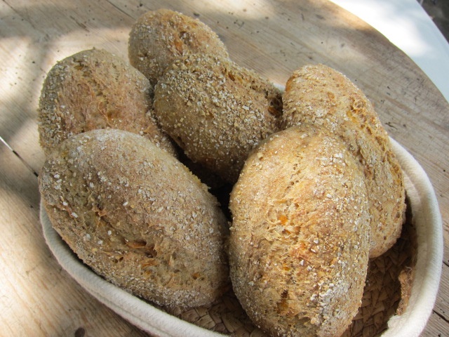 Dinkelbrötchen mit einer goldbraunen Kruste, leicht mit Haferflocken bestreut, in einem Korb auf einem Holztisch angeordnet.