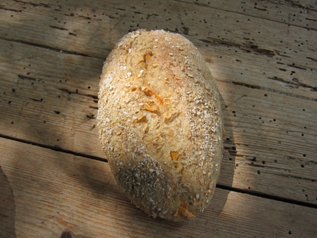Ein rustikales, rundes Brot mit einer krümeligen Oberfläche, bestreut mit Haferflocken, auf einem Holztisch.