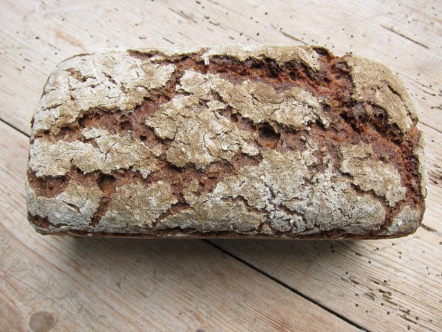 Ein rustikales Roggenbrot mit einer knusprigen Kruste und grober Textur, auf einem Holzuntergrund präsentiert.