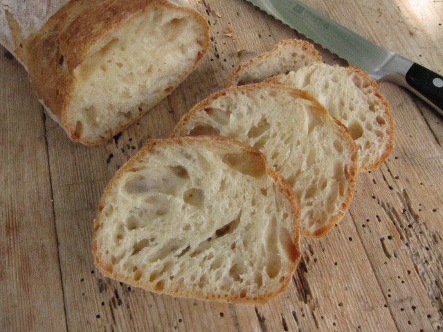 Sliced bread on a wooden surface with a knife beside it.