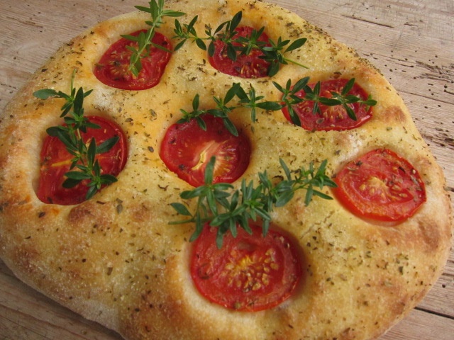 Ein frisch gebackenes Fladenbrot mit Tomatenscheiben und frischen Kräutern auf der Oberseite.