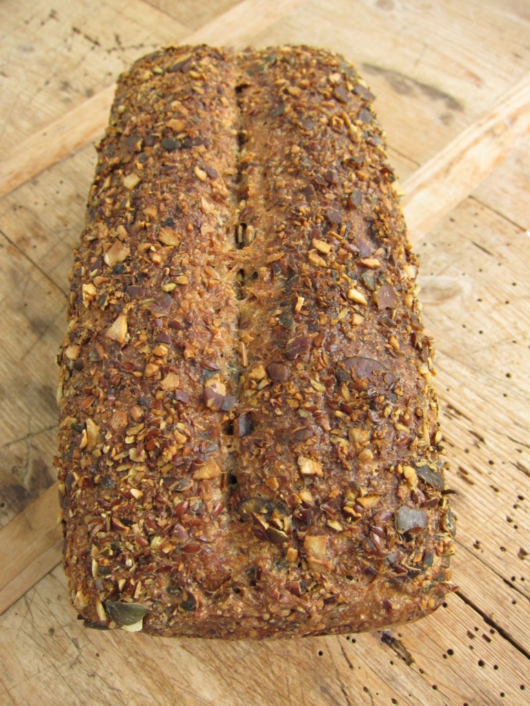 Ein frisch gebackenes Vollkornbrot mit einer knusprigen Kruste und einer Vielzahl von Samen und Nüssen auf der Oberfläche.