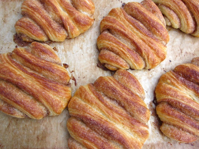 Einbleche voller Franzbrötchen mit Zimt und Zucker, die goldbraun gebacken sind.