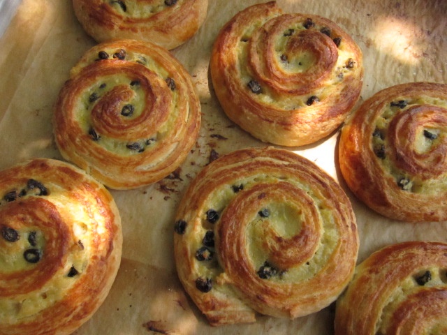 Backwaren aus Plunderteig mit einer Füllung aus Rosinen oder ähnlichen Zutaten, in spiraliger Form auf einem Backblech angeordnet.