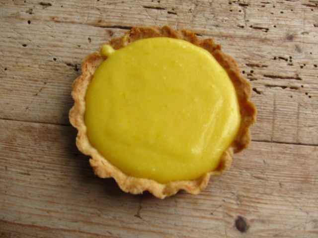 Eine kleine Tarte mit einer leuchtend gelben Füllung auf einem mürben Boden.