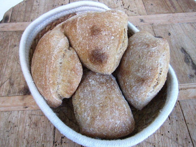 Eine Gruppe von frisch gebackenem Brot, das in einem runden Korb präsentiert wird. Die Brote sind hellbraun mit einer knackigen Kruste und einer leicht rustikalen Oberfläche.