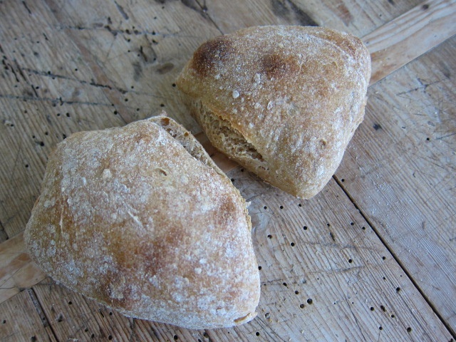 Zwei Ciabatta-Brötchen aus Rotkornweizenmehl auf einem Holztisch, mit einer leicht knusprigen Kruste und einer luftigen Krume.