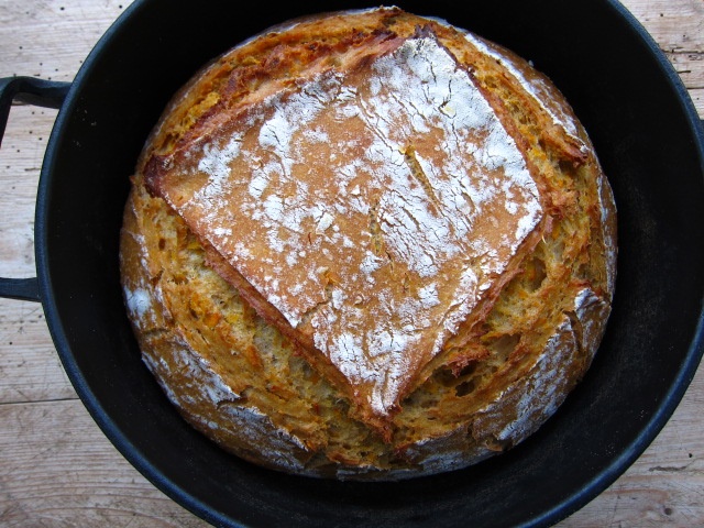 Ein frisch gebackenes Brot mit knuspriger Kruste in einem gusseisernen Topf, in einem rustikalen Holzrahmen platziert.