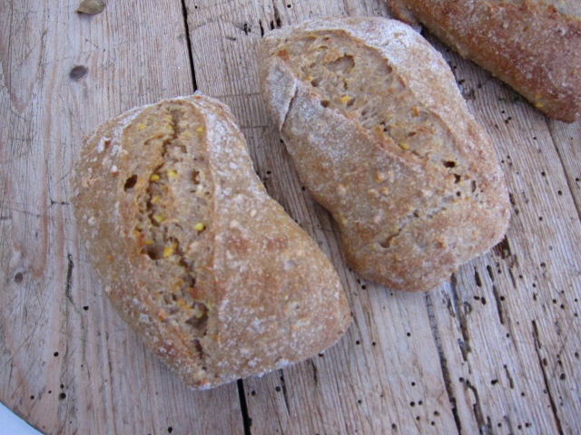 Zwei rustikale Brötchen aus Vollkornmehl mit einer knusprigen Kruste, auf einem Holztisch platziert.