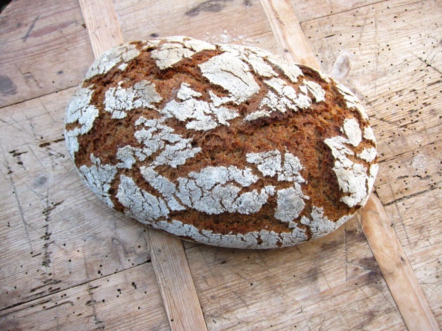 Ein frisch gebackenes Laib Brot mit rustikaler, knuspriger Kruste auf einem Holzuntergrund.