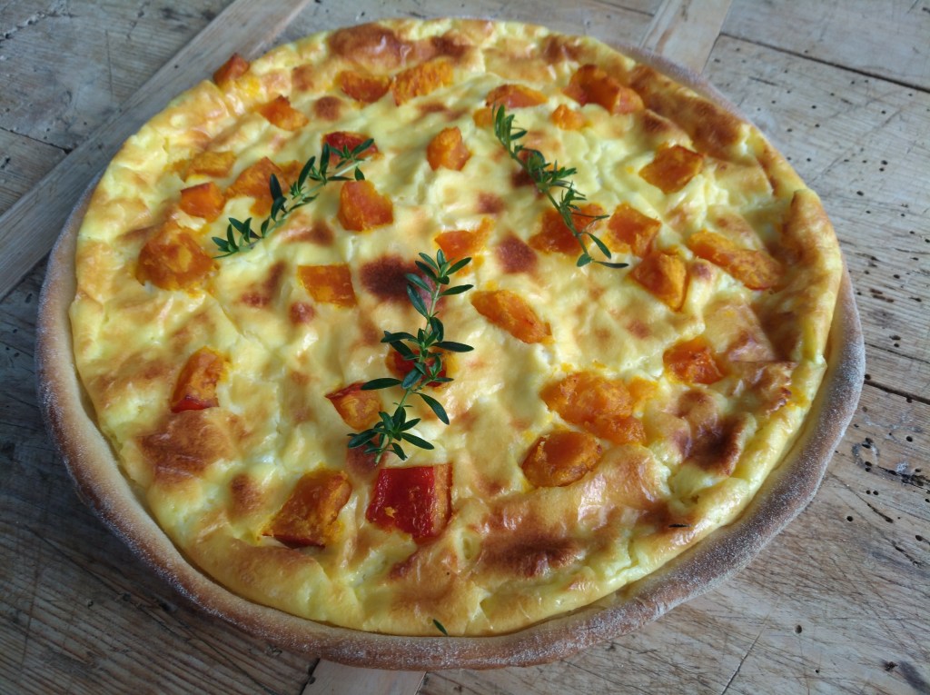 Ein herzhaftes Quiche mit Kürbisstücken und frischen Kräutern, auf einem rustikalen Holztisch serviert.