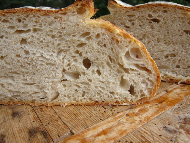 Sliced loaf of bread showing an airy crumb structure with a golden crust on a wooden cutting board.