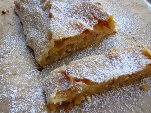 Ein Stück Apfelstrudel bestreut mit Puderzucker, auf einem Backpapier serviert.