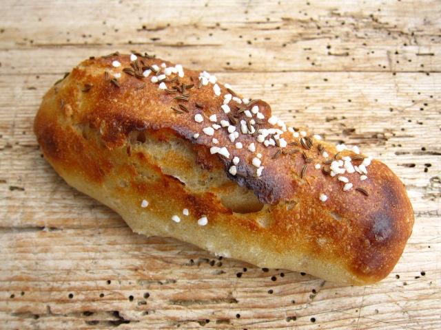 Ein frisch gebackenes Brötchen mit einer knusprigen Kruste, bestreut mit Kümmel und grobem Salz.