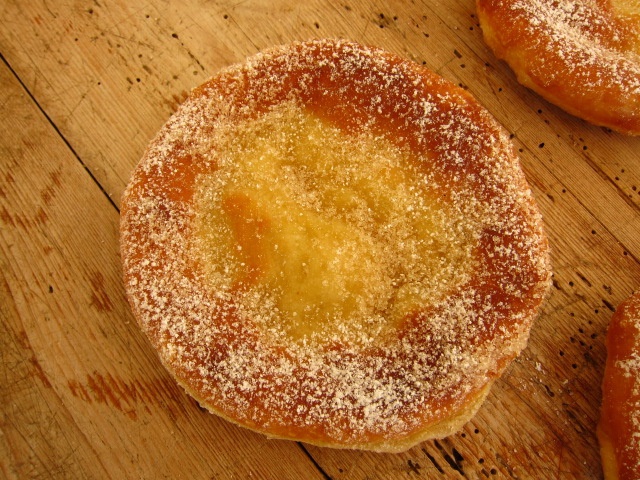 Ein rundes Gebäck mit einer glatten Oberfläche, bestreut mit Puderzucker und einer goldenen Füllung in der Mitte.