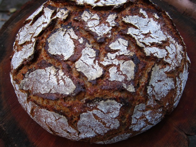 Ein rundes, rustikales Brot mit einer knusprigen, rissigen Kruste und einer groben Textur.