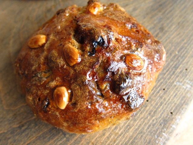 Eine süße Brötchen mit glänzender, karamellisierter Oberfläche und mandelartigen Nüssen darauf.