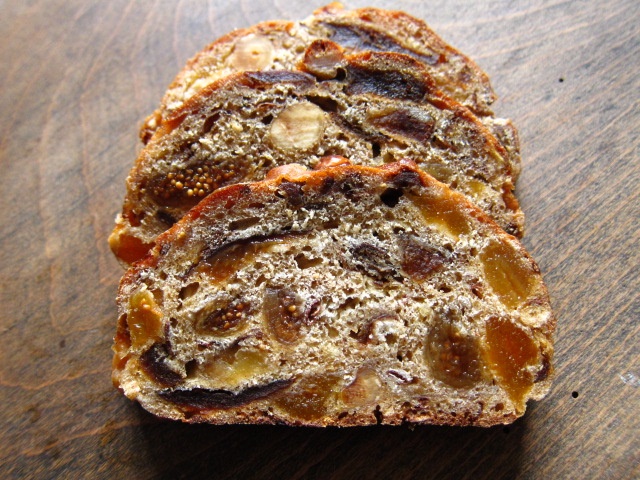 Scheiben eines fruchtigen Brotes, gefüllt mit Trockenfrüchten und Nüssen, auf einem Holzuntergrund.