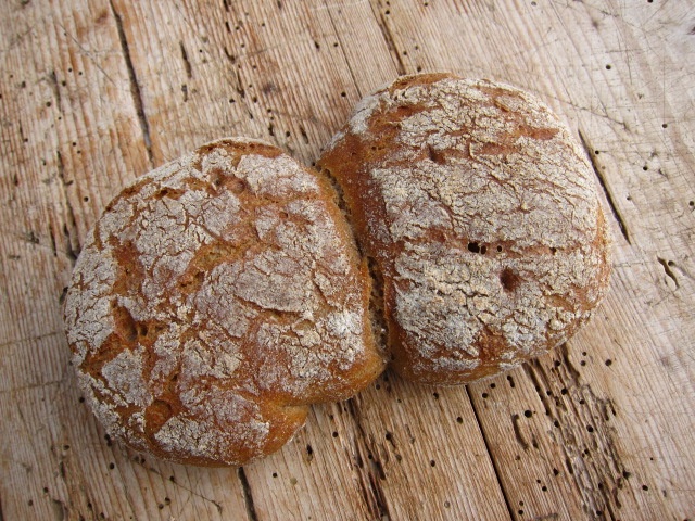 Zwei rustikale Brötchen mit einer knusprigen Oberfläche, auf einer Holzoberfläche platziert.