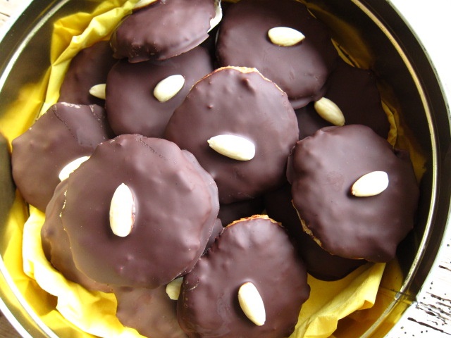 Eine Schachtel gefüllt mit runden, schokoladenüberzogenen Keksen, dekoriert mit einer Mandelnuss auf jedem Keks.