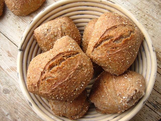Eine Schüssel mit frisch gebackenen Brötchen aus Vollkornmehl, die appetitlich in einer runden Brotform angerichtet sind.