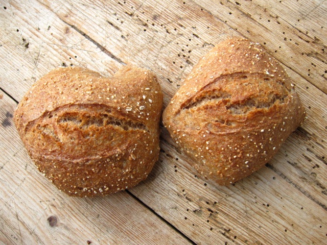 Zwei herzförmige Brötchen mit Haferflocken auf der Oberfläche, auf einer rustikalen Holzoberfläche.