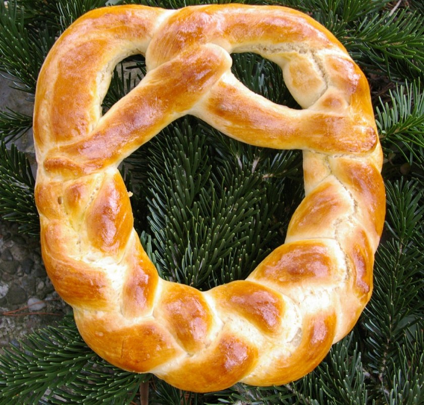 Ein goldbrauner, geflochtener Hefezopf auf einem Hintergrund aus grünen Tannennadeln.