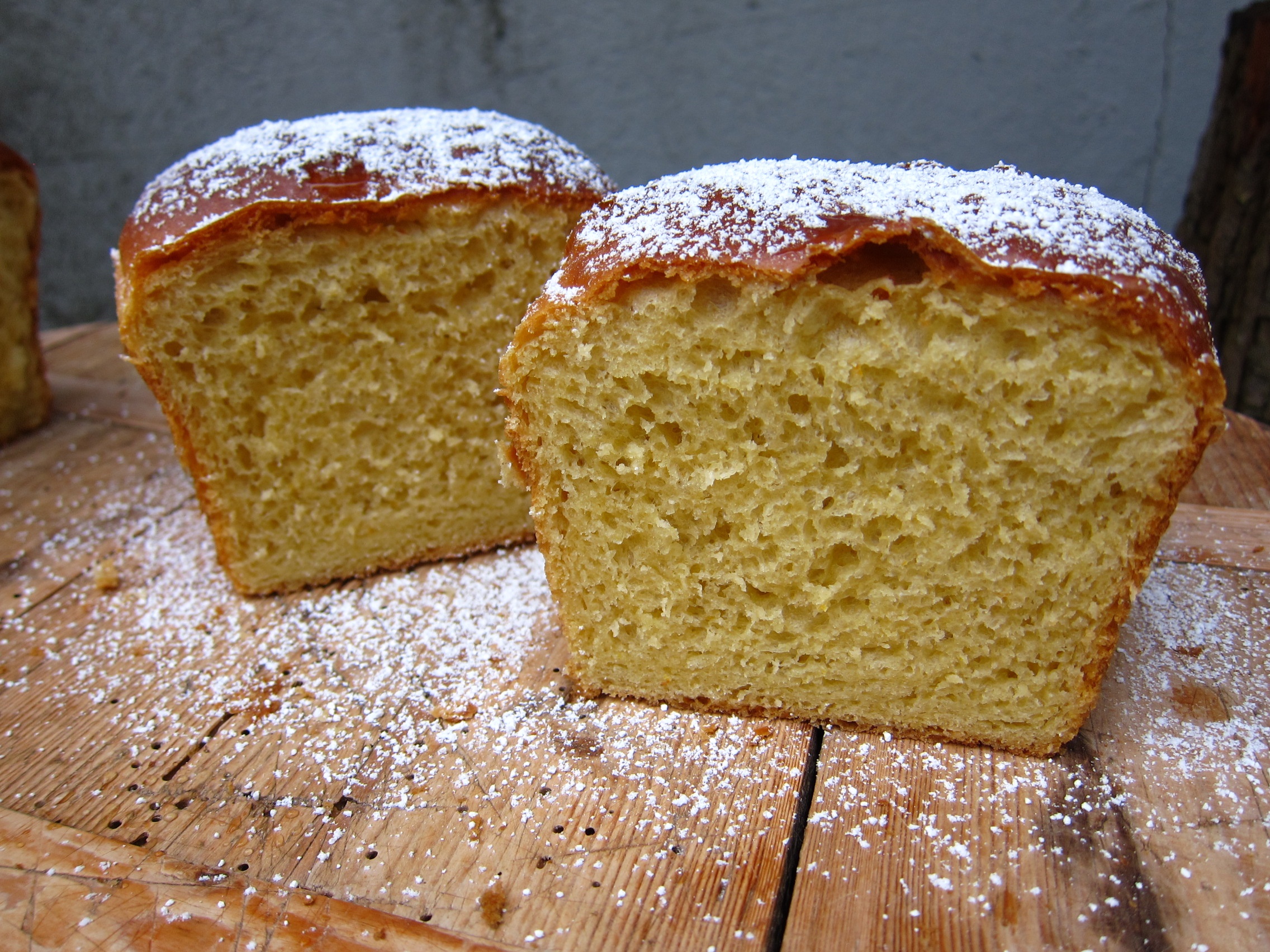 Aufgeschnittenes, leichtes Brot mit einer goldbraunen Kruste und Puderzucker bestreut, auf einem Holzbrett.