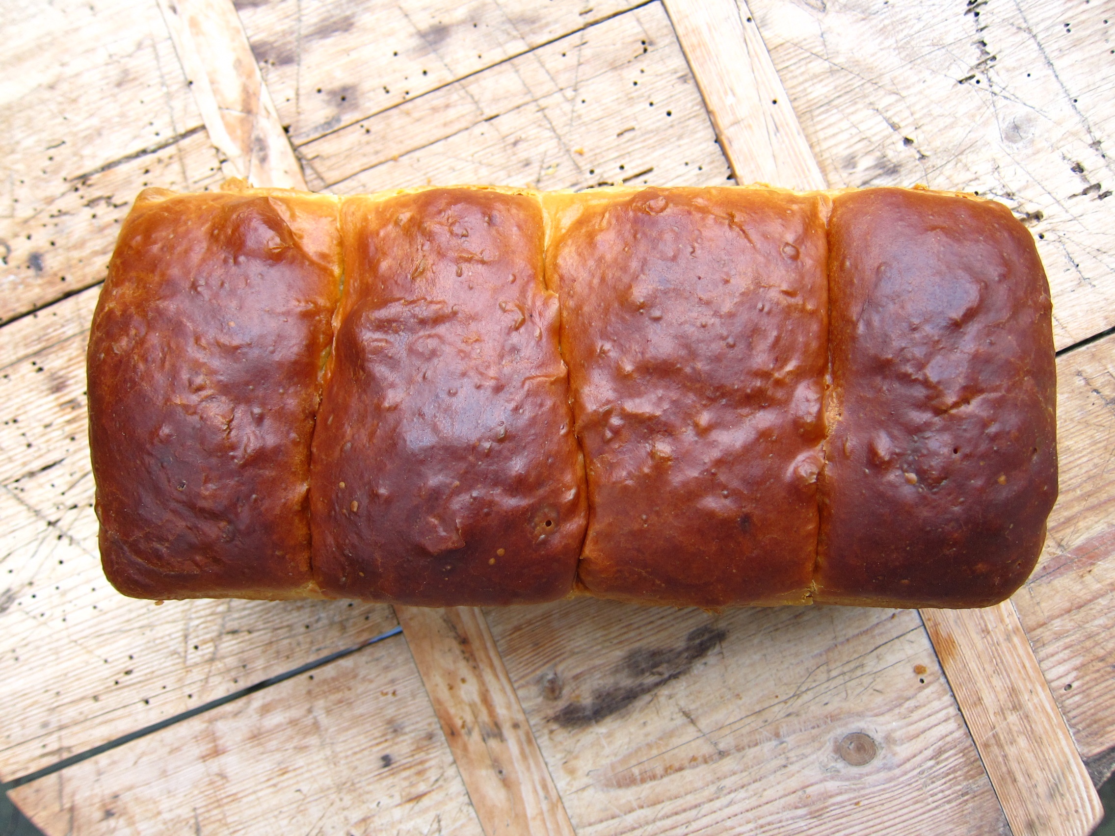 Ein frisch gebackenes, goldbraunes Brot mit glänzender Kruste, auf einer Holzoberfläche platziert.