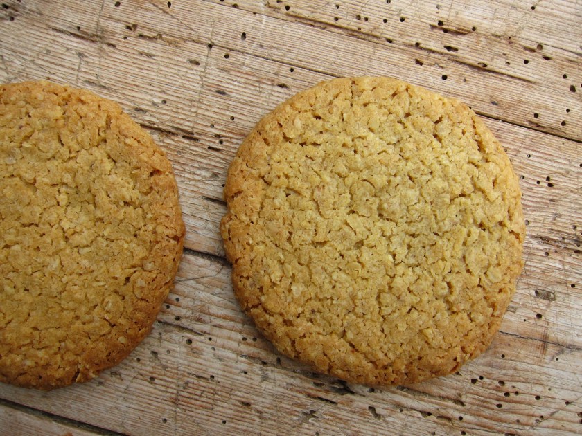 Zwei goldene Haferkekse auf einem Holzuntergrund.