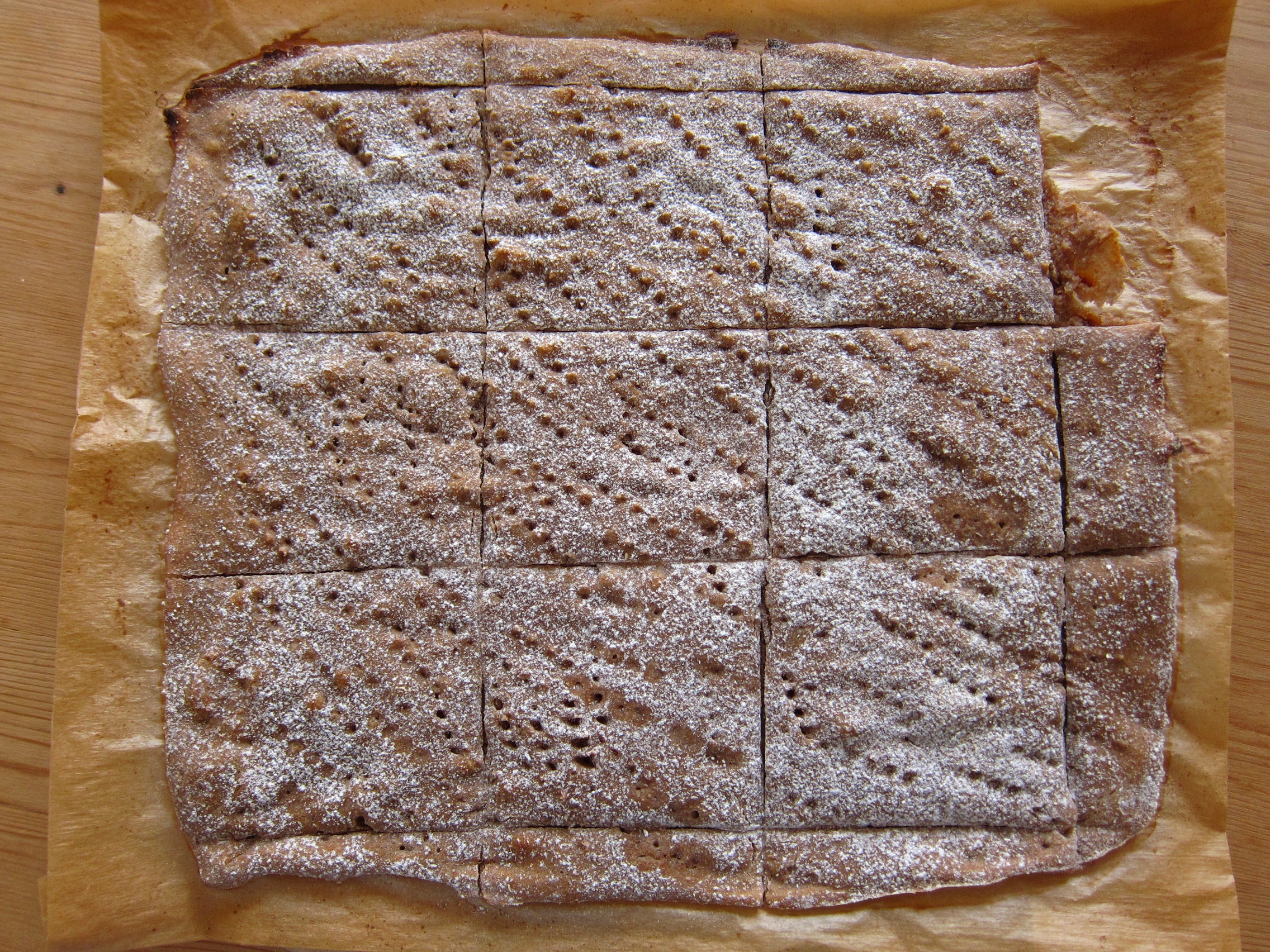 Ein rechteckiger gebackener Keks oder Kuchen, mit Puderzucker bestäubt und in gleichmäßige Stücke geschnitten, auf Backpapier gelegt.