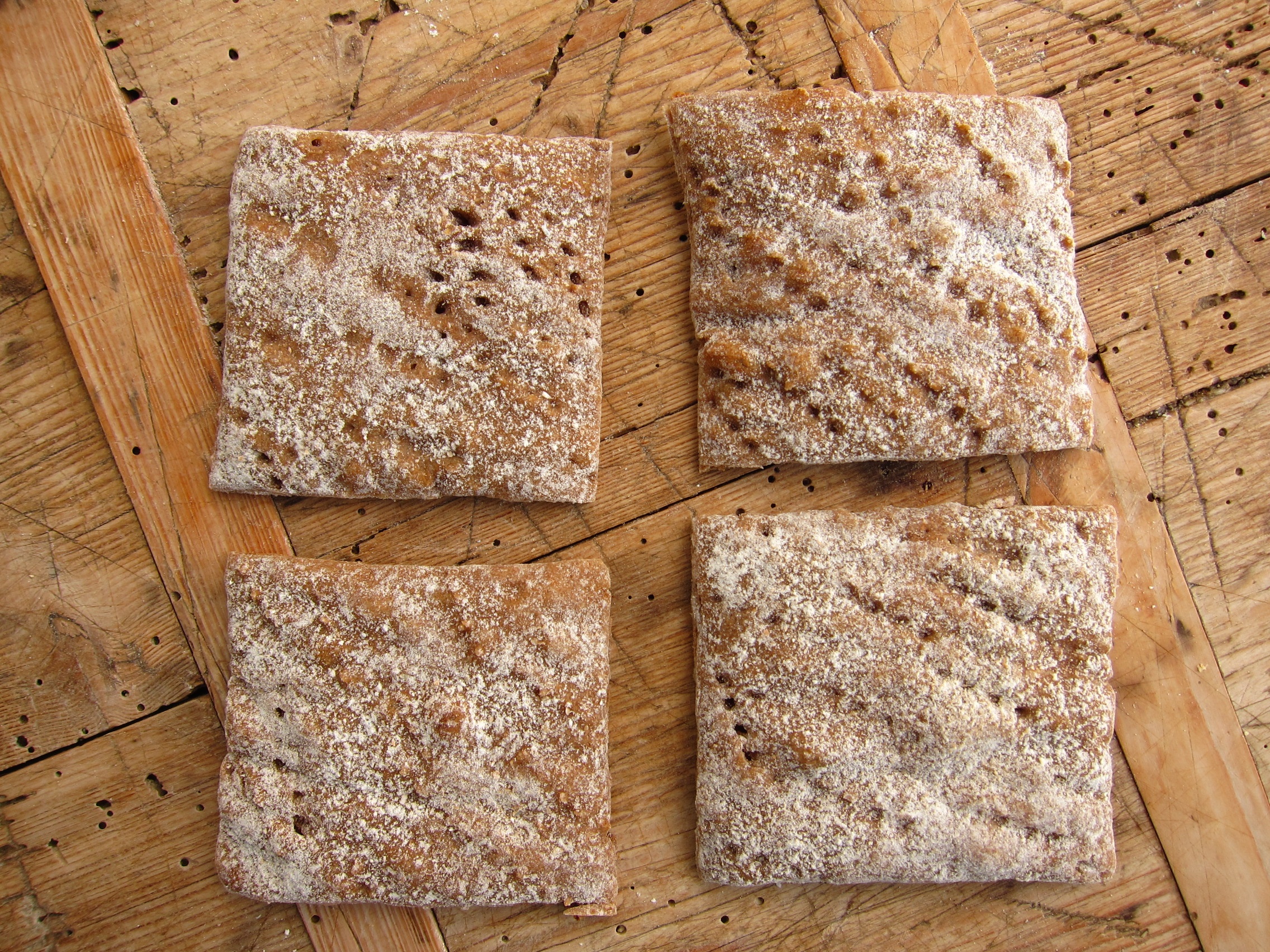 Vier quadratische Stücke Gebäck auf einer Holzunterlage, bestäubt mit Mehl.