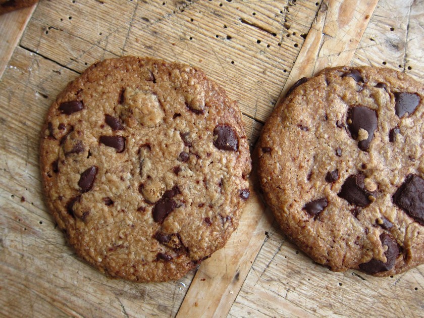 Zwei große Schokoladenkekse auf einer Holzoberfläche, mit schokoladigen Stücken sichtbar.