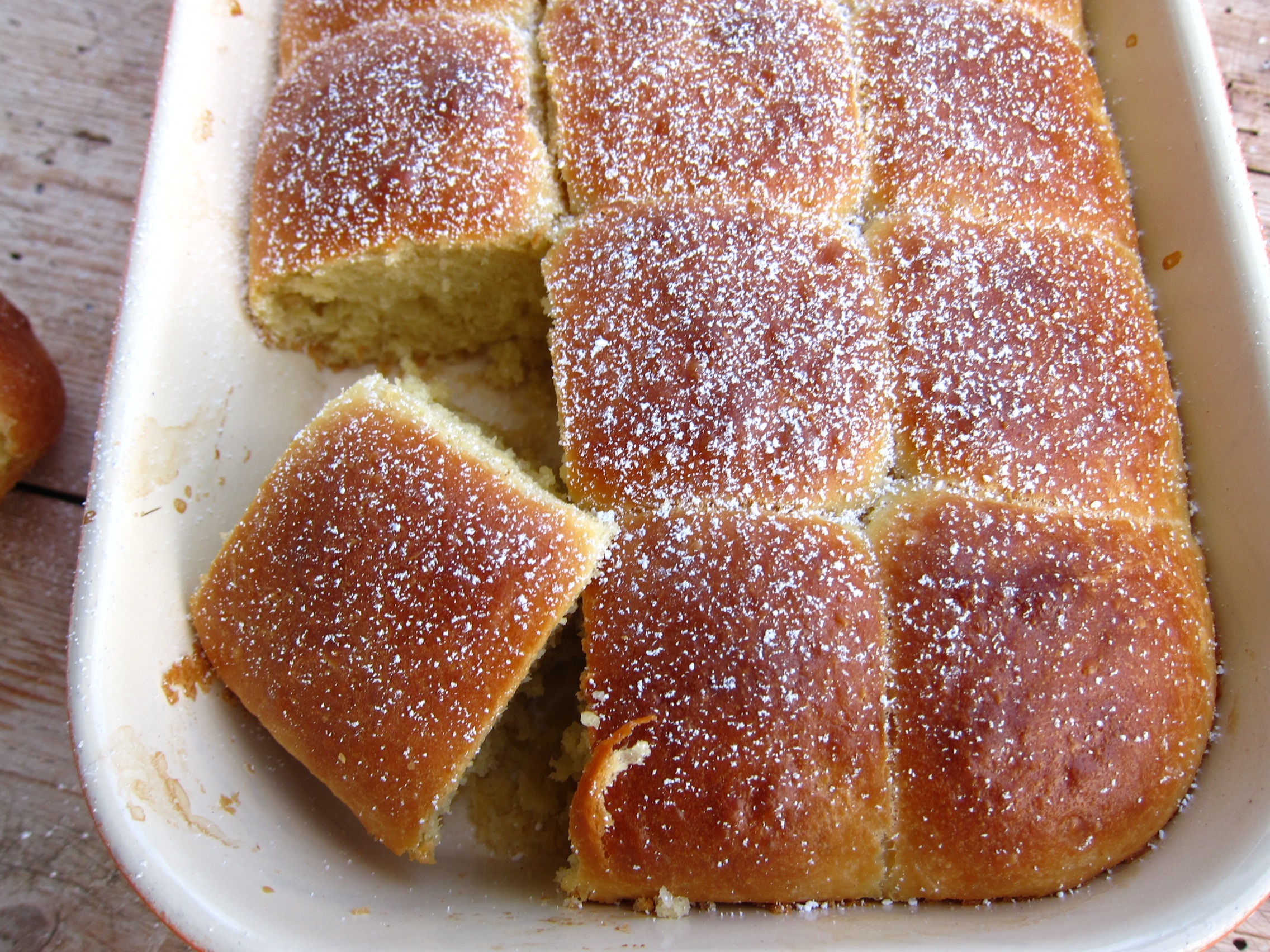 Ein Blech von frisch gebackenem, fluffigem Brot mit einer goldbraunen Kruste und Puderzucker bestreut.