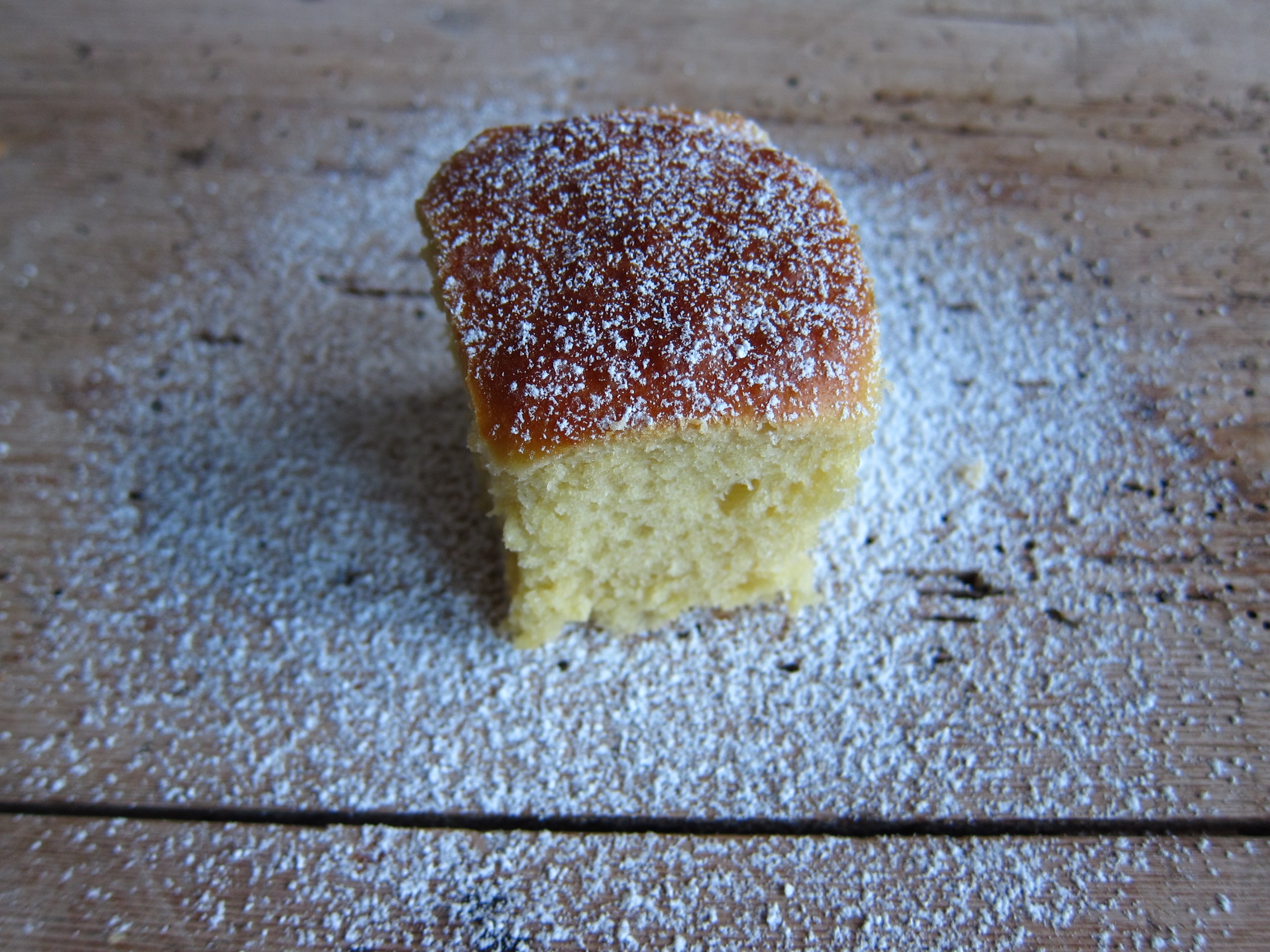 Ein Stück Kuchen mit einer dünnen Schicht Puderzucker auf einer Holzoberfläche.