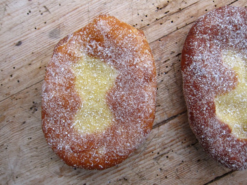 Zwei Hefeteiggebäcke, mit Puderzucker bestäubt, auf einem Holzuntergrund.