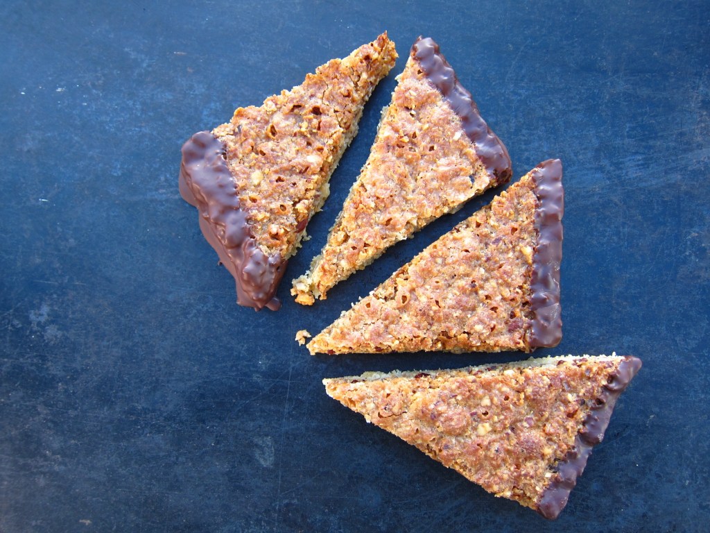 Drei Stücke Schokoladenkekse auf einem dunklen Untergrund, mit einer Schokoladenglasur an den Kanten.