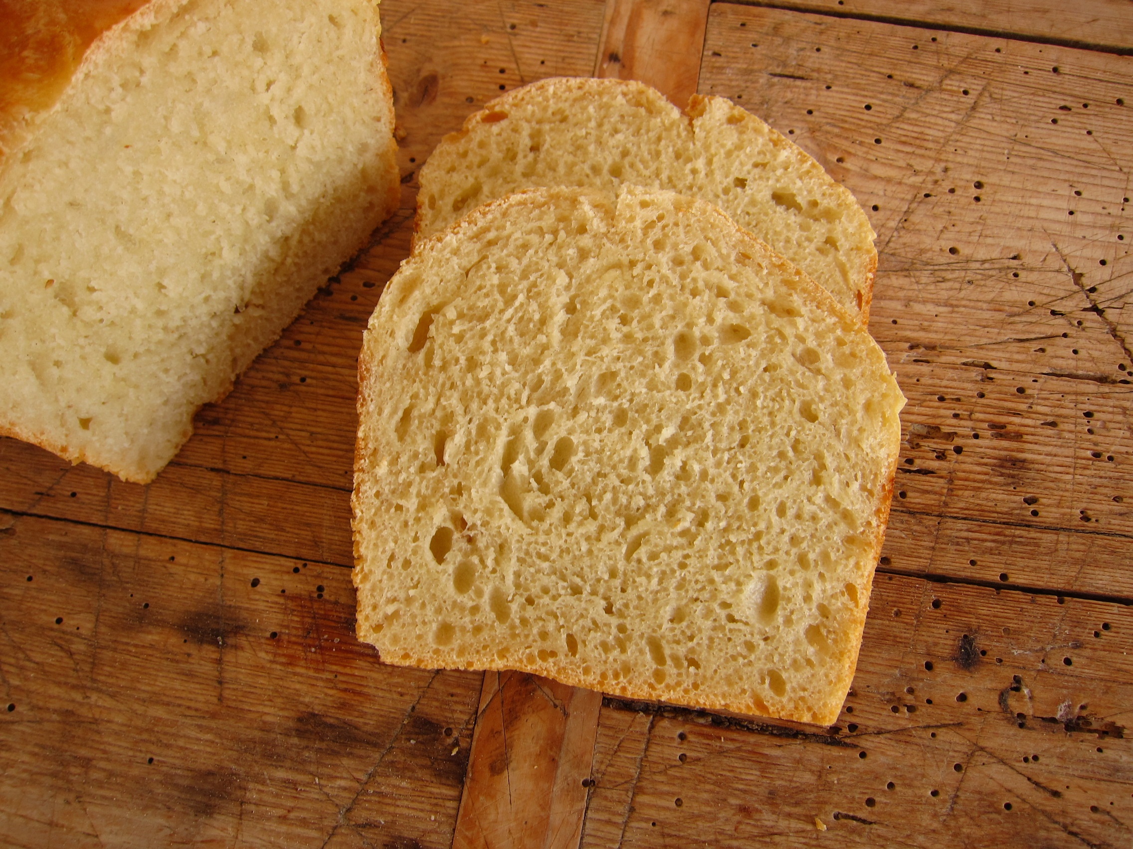 Aufgeschnittenes, frisch gebackenes Brot auf einem Holzbrett, das eine goldbraune Kruste und eine luftige, helle Innenstruktur zeigt.