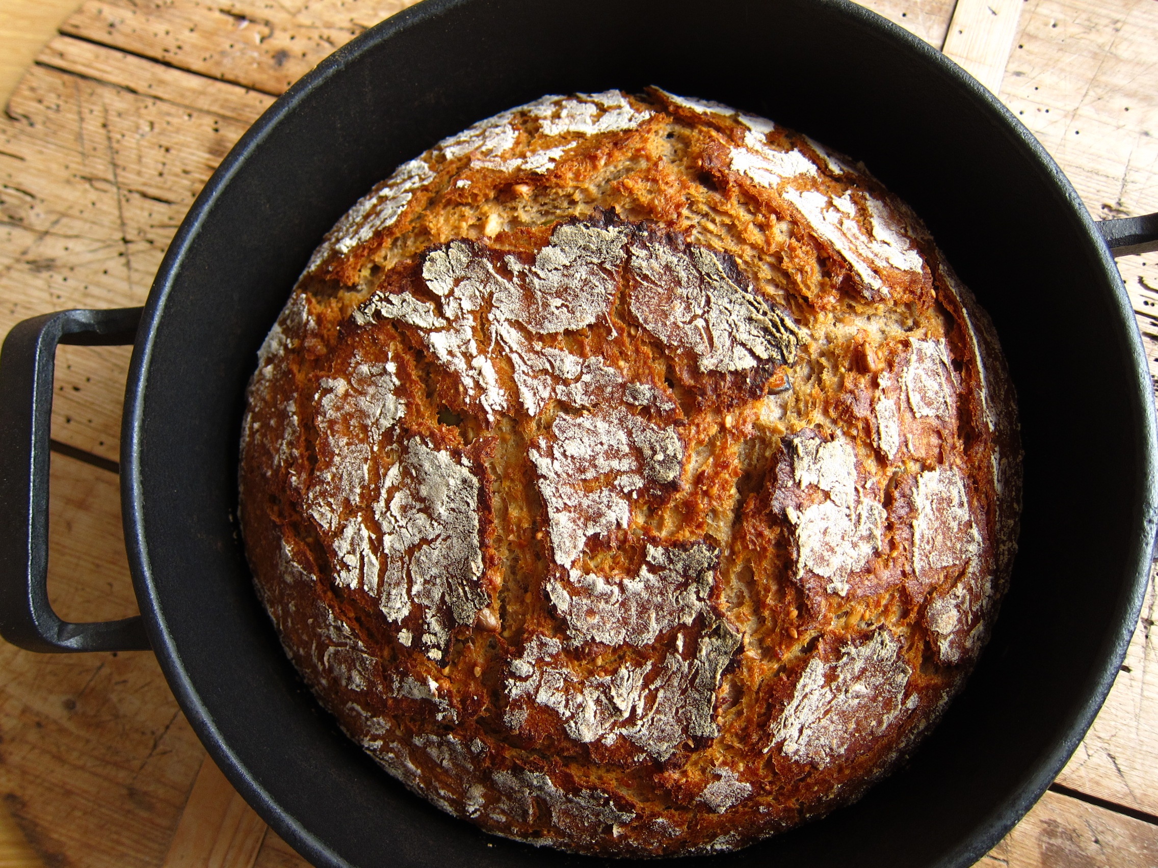 Ein frisch gebackenes Brot mit einer rustikalen, goldbraunen Kruste, serviert in einem gusseisernen Topf.