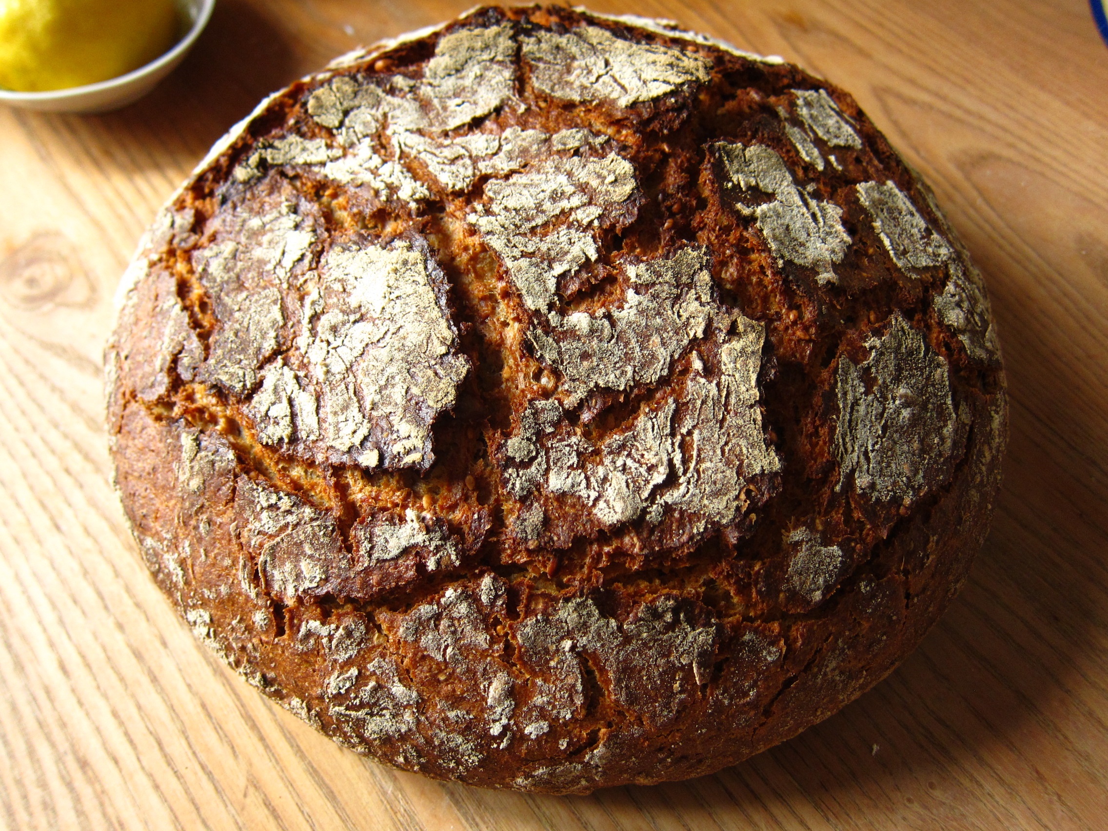 Ein frisch gebackenes Brot mit einer rustikalen, knusprigen Kruste und einer goldenen, unregelmäßigen Oberfläche, auf einem Holzuntergrund.